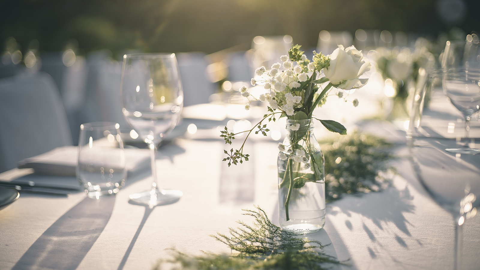 Beautiful outdoor table setting with white flowers for a dinner, wedding reception or other festive event.