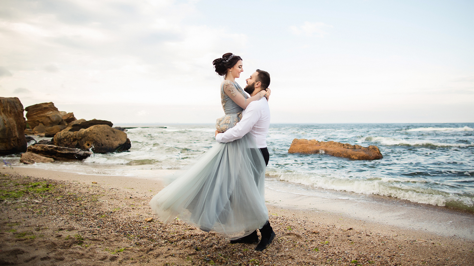 Wedding. Wedding by the sea. Young couple in love, bearded groom and bride in wedding dress at the seaside. Couple in love walking around the sea and the rocks near the place of the wedding ceremony.