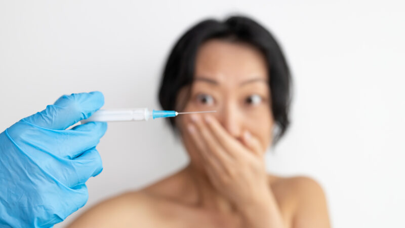 Nurse hand with syringe needle and asian woman fear of injections phobia concept against white background. Focus on hand.