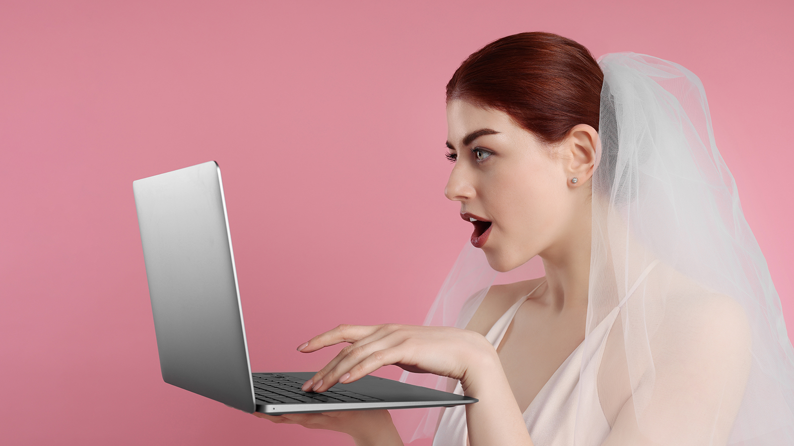 Surprised bride using laptop on pink background