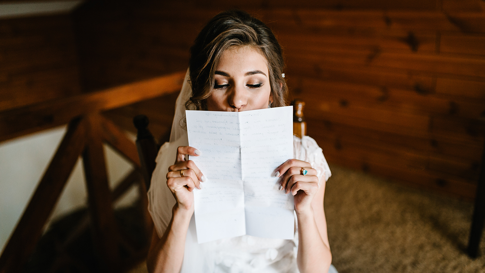 Beautiful bride reading, kissing letter from the groom for love. Bride's tears of happiness, joy. The bride sits at window and reads letter to groom. Wedding vows. Morning of the bride.