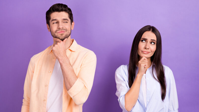 Photo of unsure funny husband wife dressed shirts looking empty space arm chin isolated purple color background