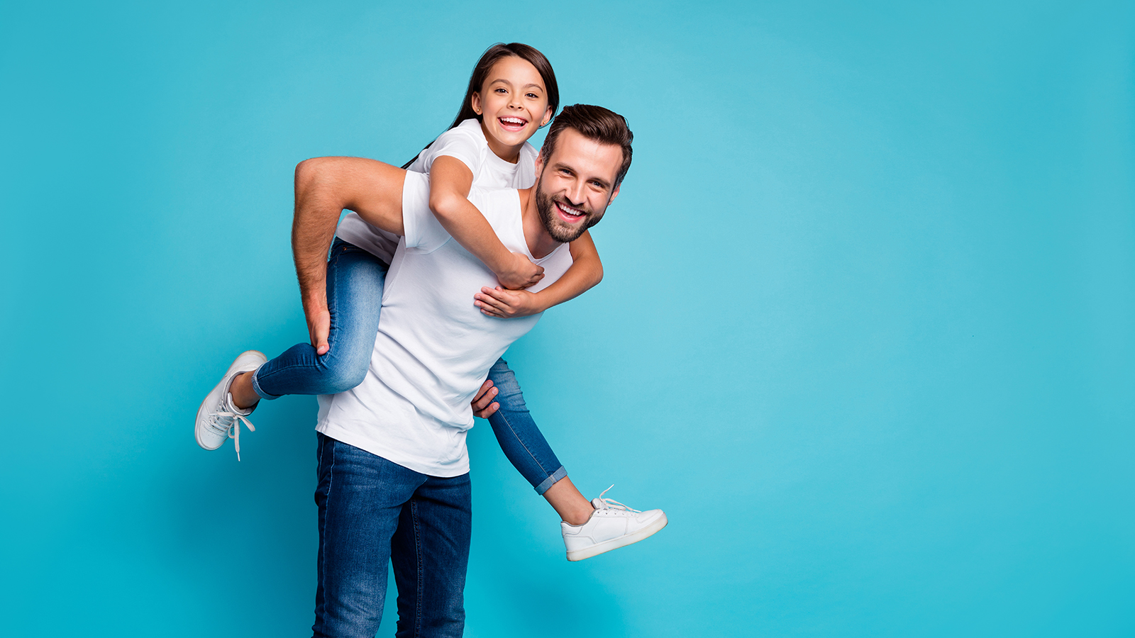 Portrait of cheerful people laughing piggyback wearing white t-shirt denim jeans isolated over blue background