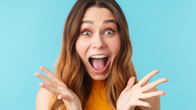 Portrait of a cheerful excited pretty young girl standing isolated over blue background, looking at camera