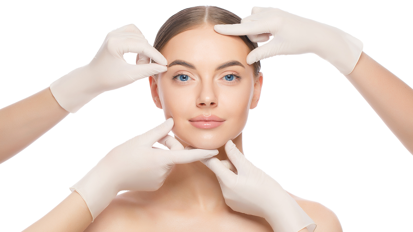 Close-up portrait of young female standing with naked skin, face is touched by doctors in gloves, preparing her for plastic surgery procedures, isolated on white background