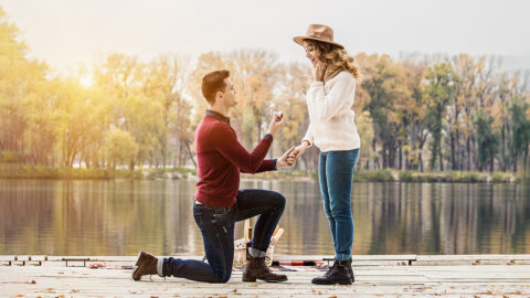 Marry me. Horizontal shot of young man in casual clothing standing on one knee and holding engagement ring while making wedding proposal to his beautiful girlfriend. Engagement of young couple.