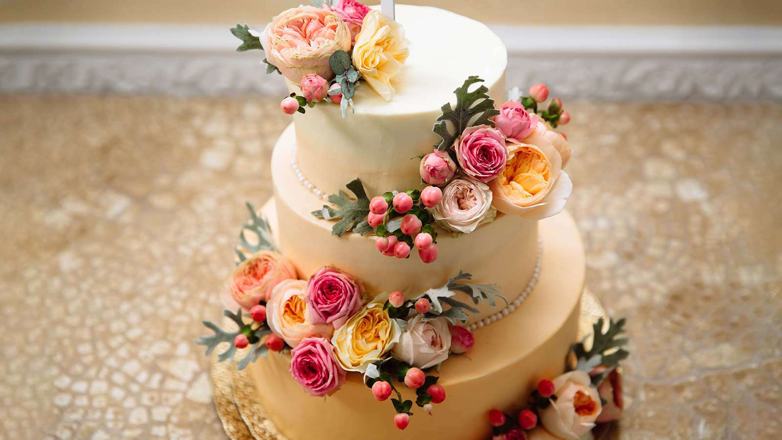 Photo of wedding cake with gold plating. The three-tiered cake for the wedding is painted with beautiful large live flowers.