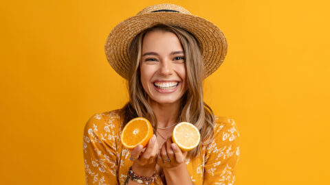 beautiful attractive stylish woman in yellow dress and straw hat holding lemons posing on yellow background isolated, vitamin fruit diet skin natural