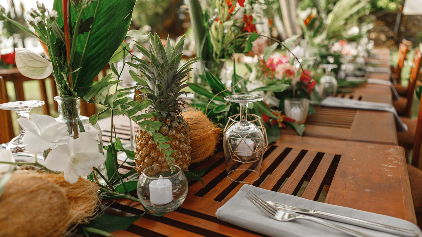 Served tables for wedding banquet with plates placed on palm leaves in restaurant. Served table for a wedding dinner in boho chic style. Decor from fresh flowers of greenery, pineapples and coconuts.