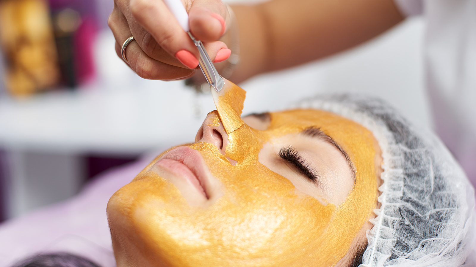 Macro photography of the hand of the beautician with the help of a special brush puts on the face of the girl a golden mask in the spa