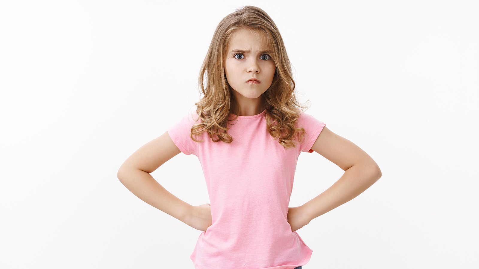 Offended cute sulking young blond little girl kid looking upset, frowning hold hands hips insulted, stare camera disappointed, waiting apologies, jealous brother ate her sweets, white background