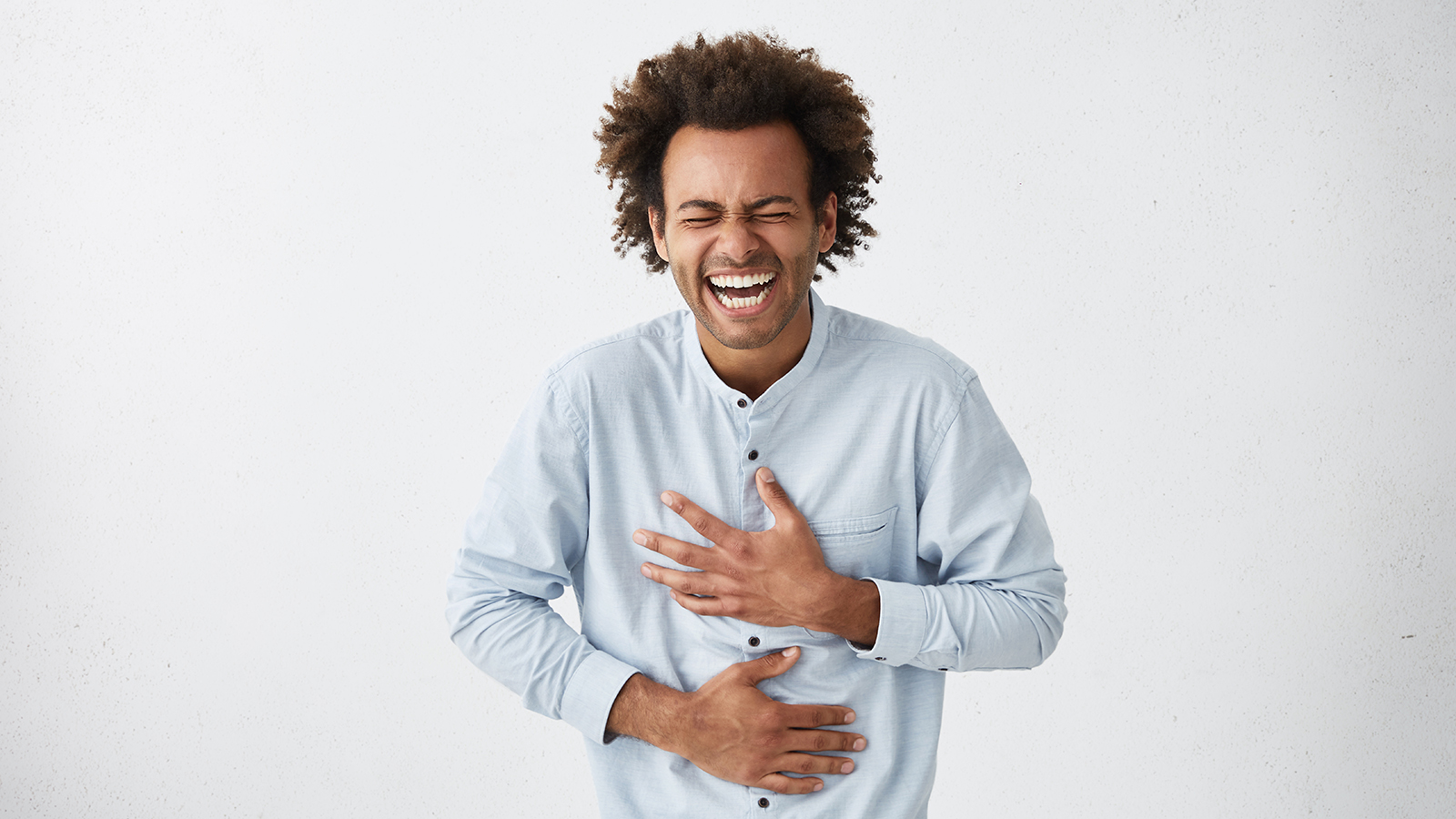 Positive and joyful Afro American male with fine crop of hair bursting into laughing holding his hands on stomach can`t stopping laughing after hearing funny anecdote. Positive emotions and humour