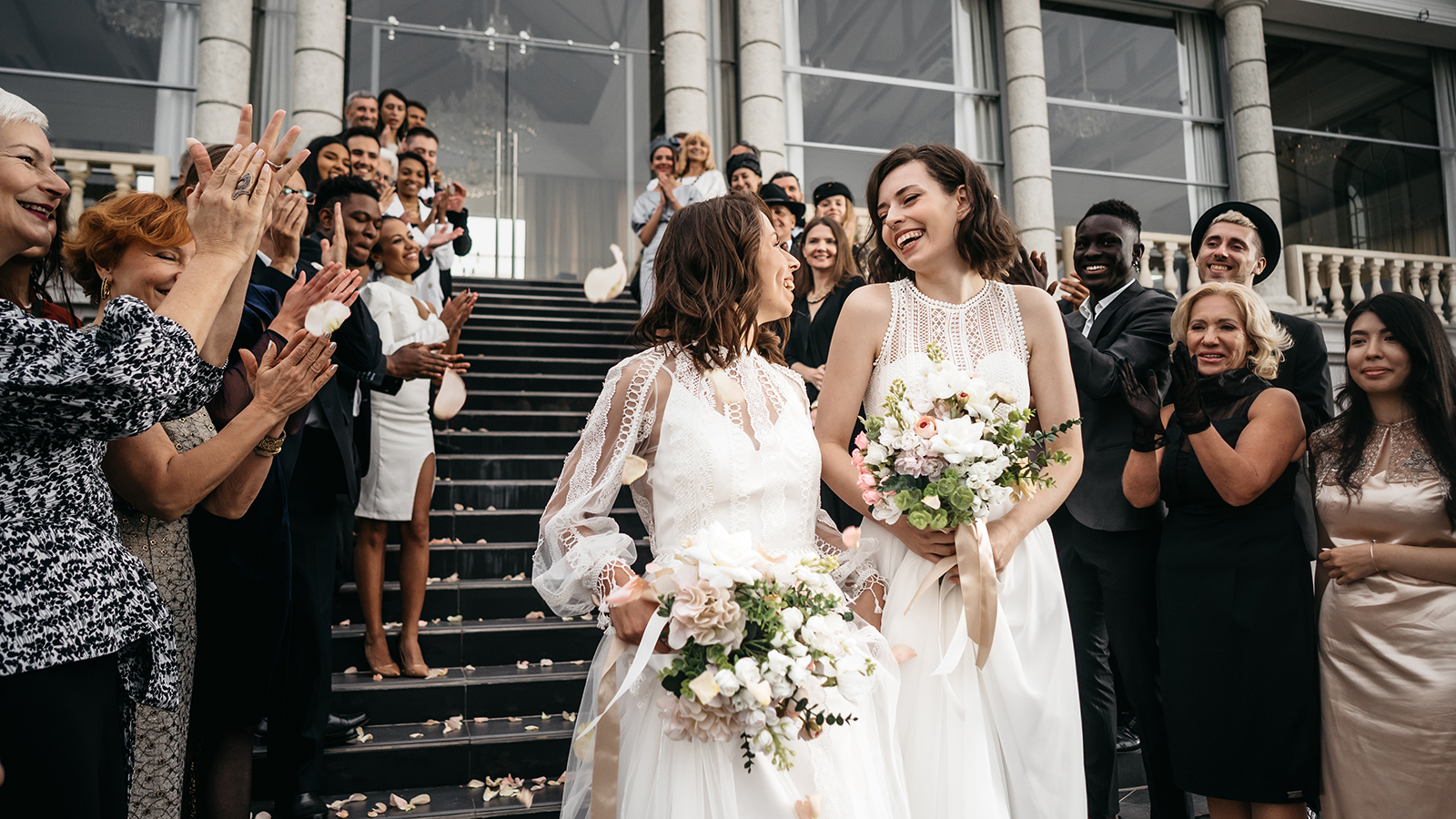 Candid shot of two female lesbian LGBT brides walking down the stairs during their wedding ceremony, guest clapping and cheering