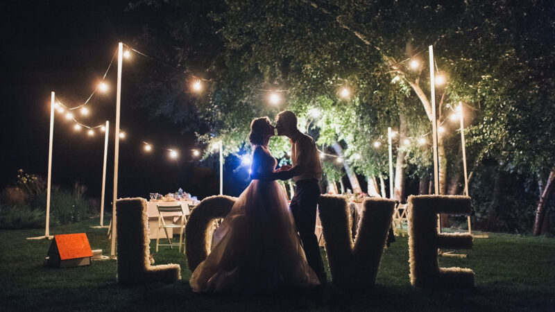 Beautiful newlyweds kiss tenderly at a wedding party with lamps. Stylish wedding ceremony. Love in the frame. Designer letters. Grain, film effect.