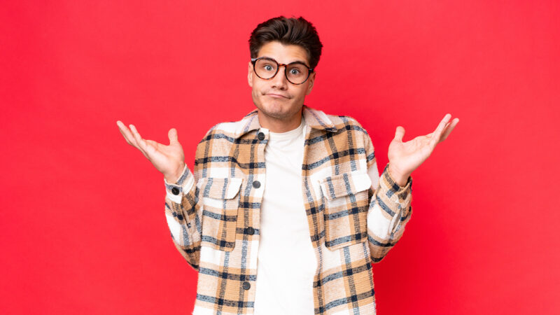 Young caucasian handsome man isolated on red background having doubts while raising hands
