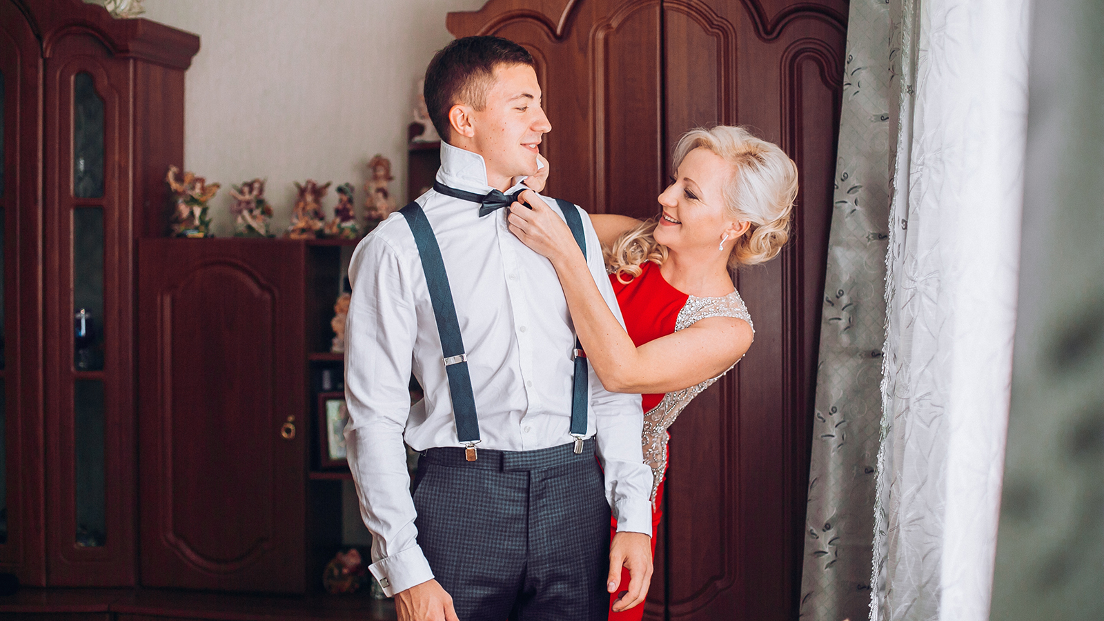 Mother is helping with a bow-tie to her son before wedding ceremony.