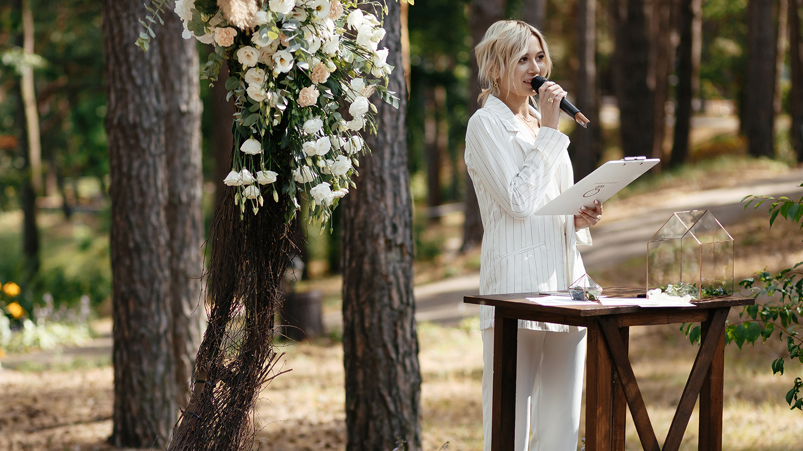 Master of wedding ceremony speeching on microphone on background wedding arch and trees.
