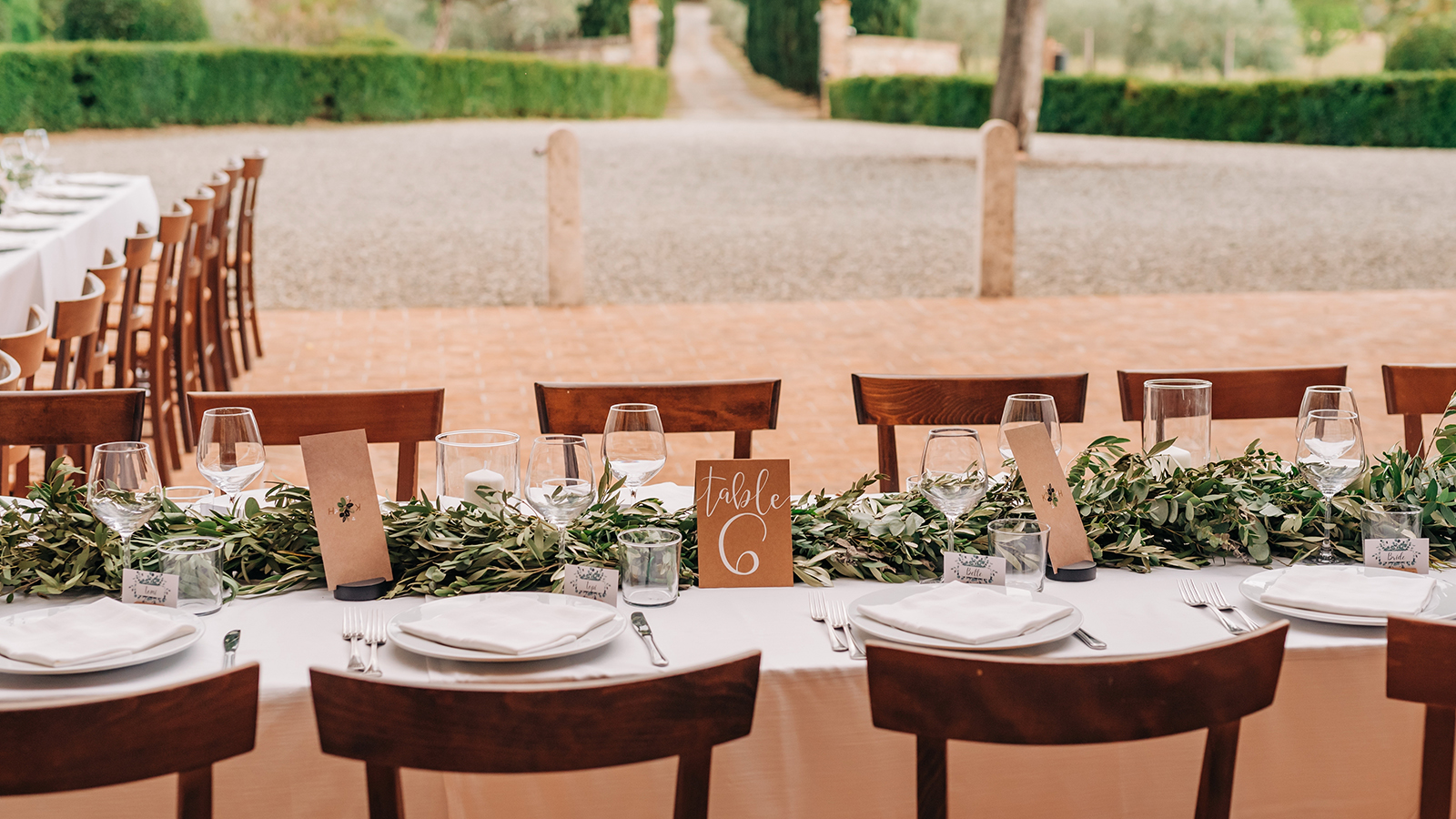 Wedding decor for dinner in a villa in nature. Rectangular long tables are decorated with greenery and olive branches. Rustic wedding decor