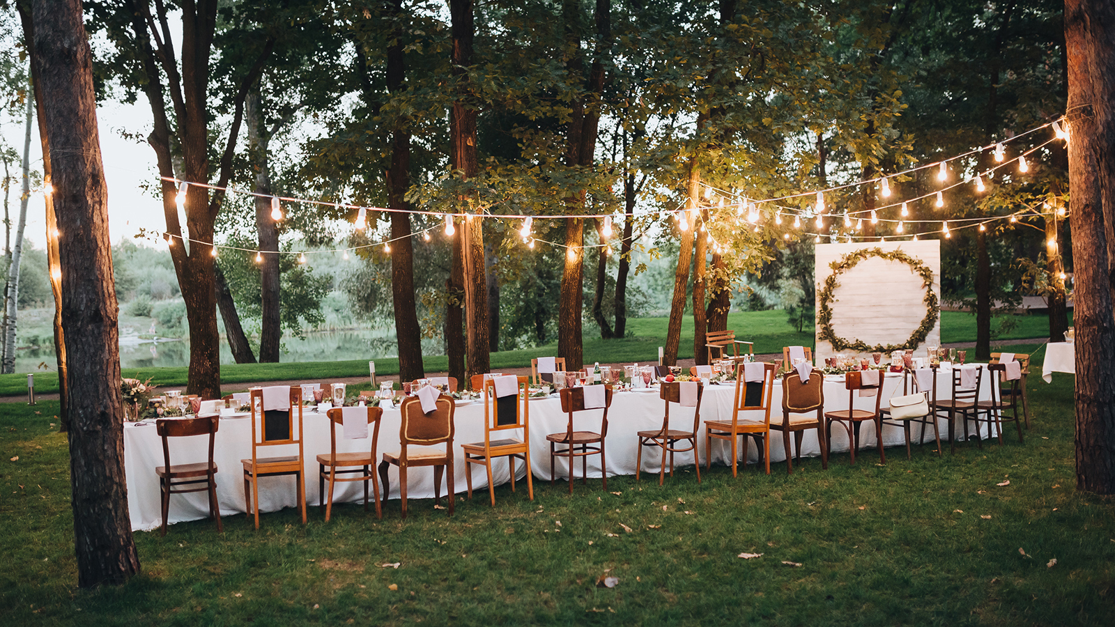 Festive table served dishes and decorated with branches of greenery, stands on green grass in the area of wedding party