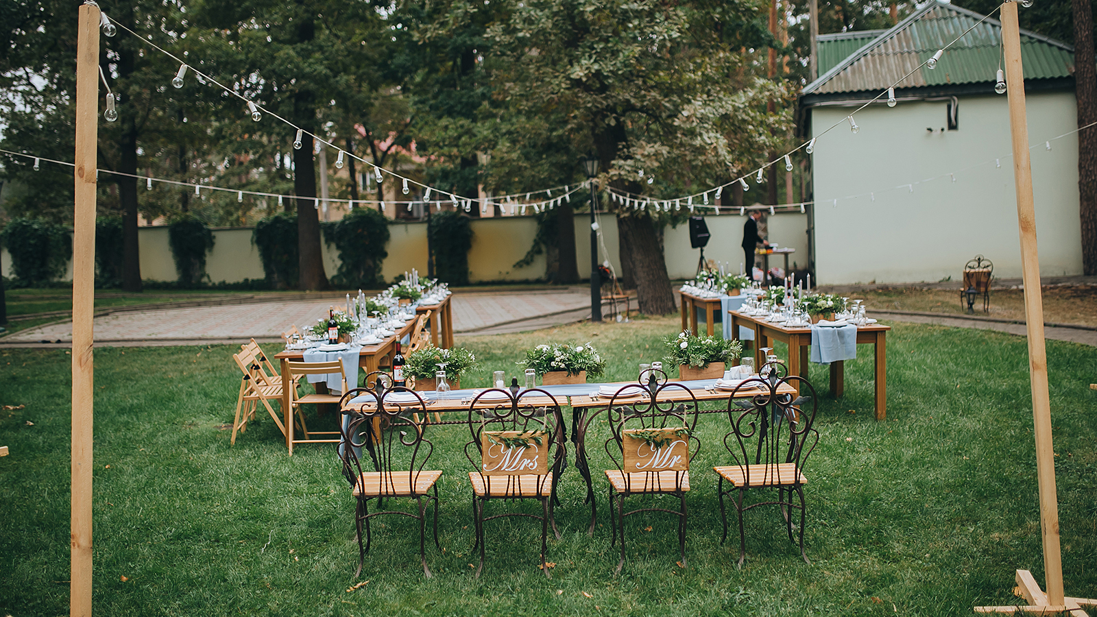 Wedding. Banquet. Chairs and honeymooners table decorated with candles, served with cutlery and crockery and covered with a tablecloth. The table stands on a green lawn in the backyard banquet area