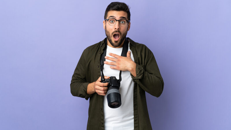 Photographer man over isolated purple background surprised and shocked while looking right