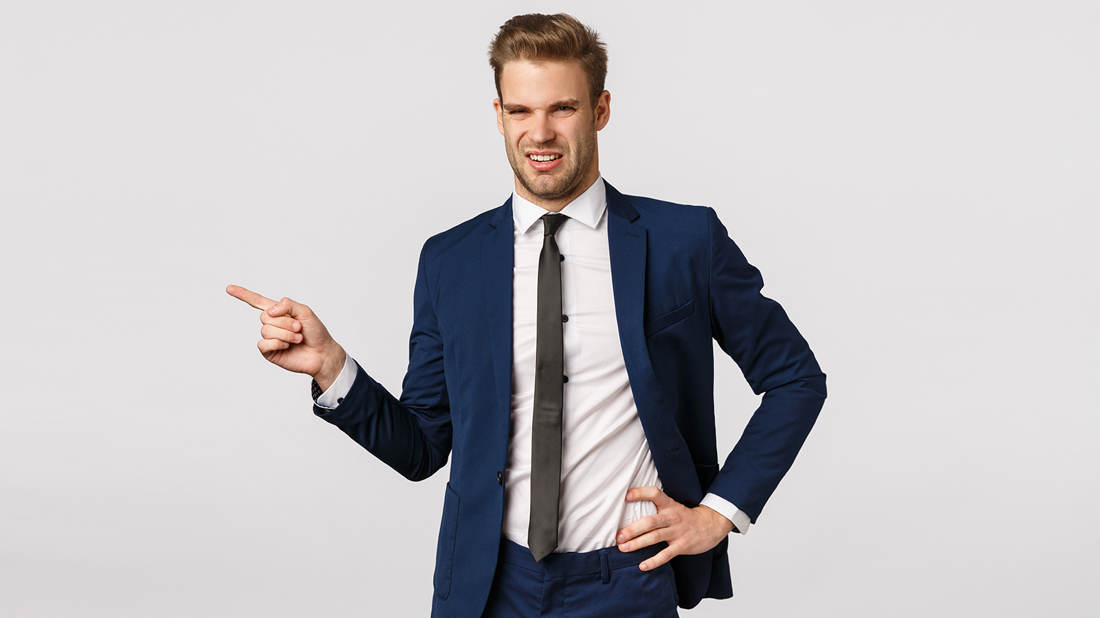 Eeew disgusting scene. Young male entrepreneur in classic suit, pointing left and grimacing with aversion, cringe from reek, bad smell, or unappealing person, standing reluctant white background