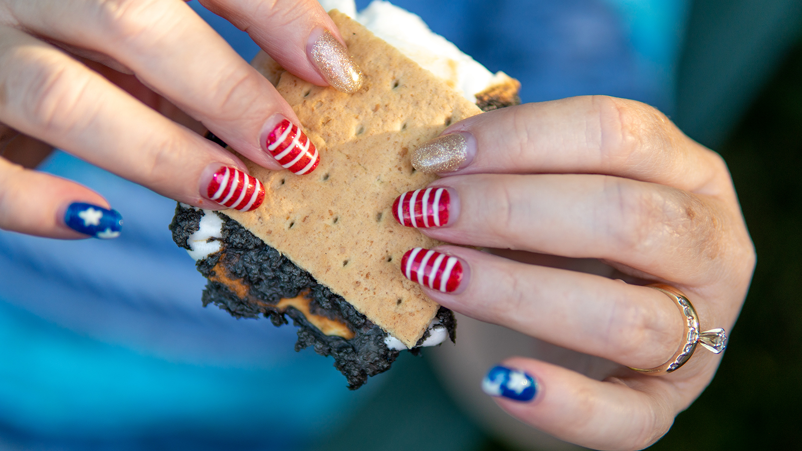 A woman holds a s'more with patriotic nails.