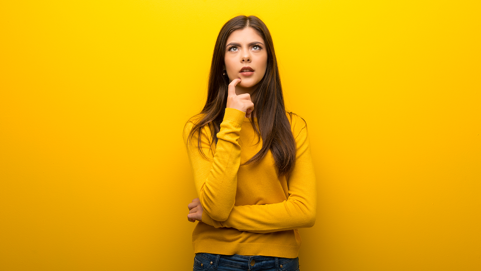 Teenager girl on vibrant yellow background having doubts while looking up