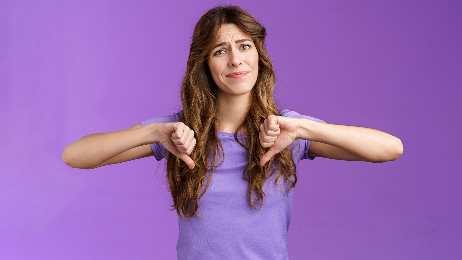 Disappointed displeased pity girl show thumbs down grimace dislike express negative opinion thumbs down gesture apologizing giving bad feedback stand purple background unimpressed.