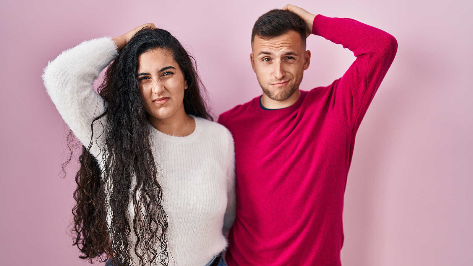 Young hispanic couple standing over pink background confuse and wondering about question. uncertain with doubt, thinking with hand on head. pensive concept.