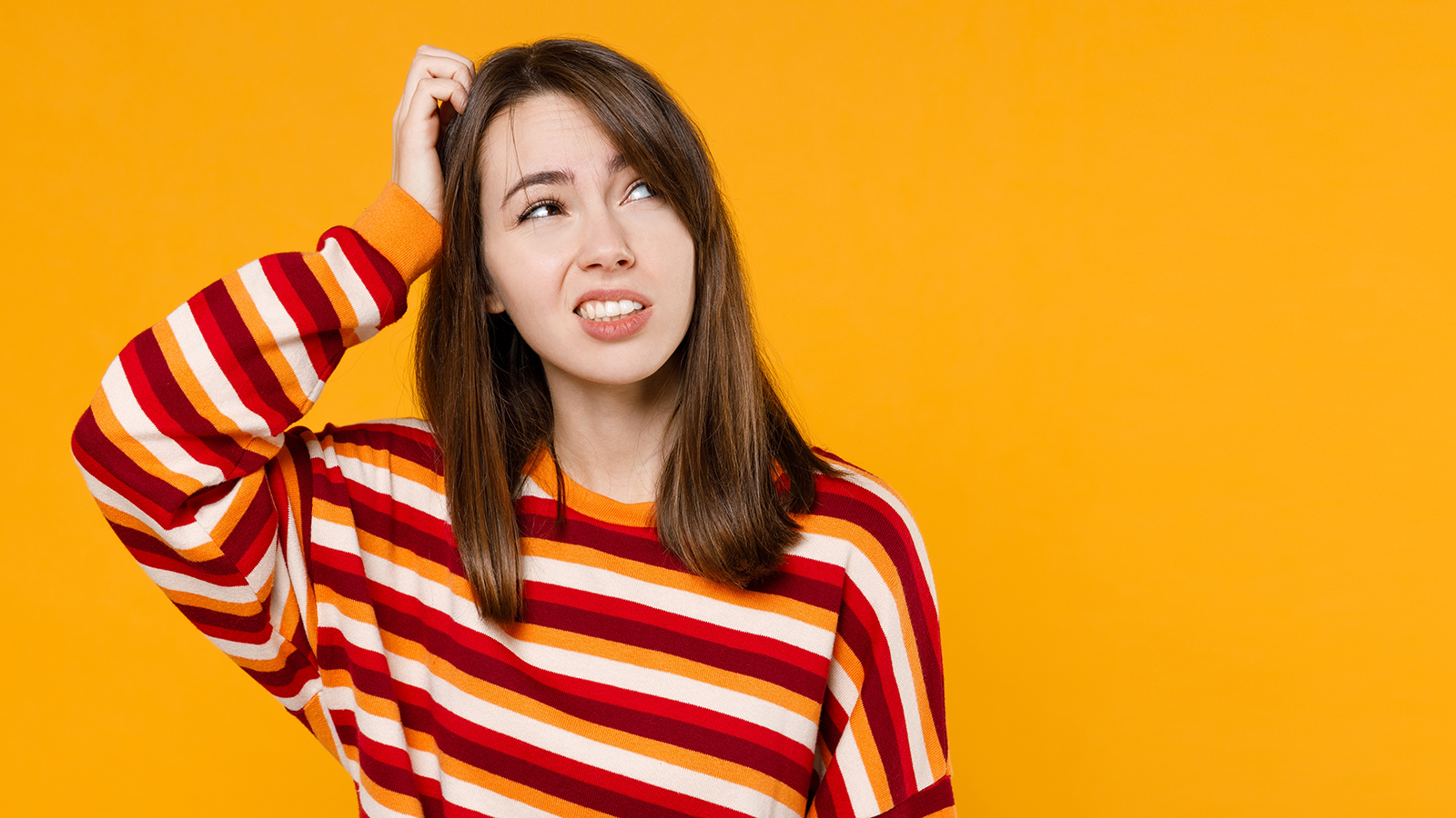 Young sad puzzled caucasian woman in red striped sweatshirt look aside on workspace area mock up hold scratch head fingers isolated on plain yellow background studio portrait. People lifestyle concept