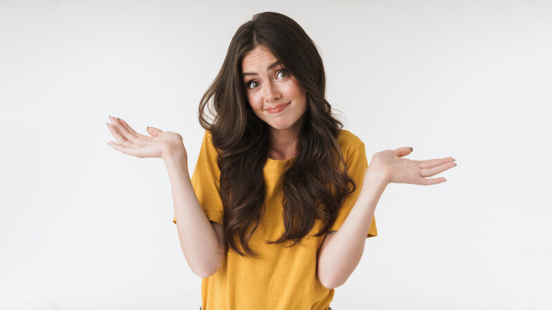 Image of caucasian brunette woman wearing casual t-shirt shrugging and throwing up her hands isolated over white background