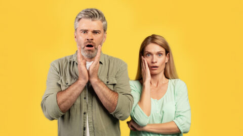 Shocked european middle aged husband and wife with open mouth looking at camera, posing on yellow background. Reaction to news, huge sale, ad and offer, facial expression
