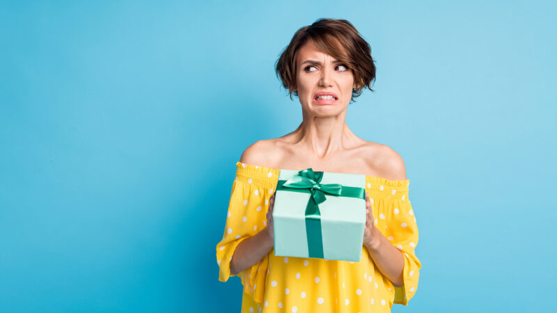 Photo of disgusted young woman hold dislike gift look empty space bad mood isolated on blue color background