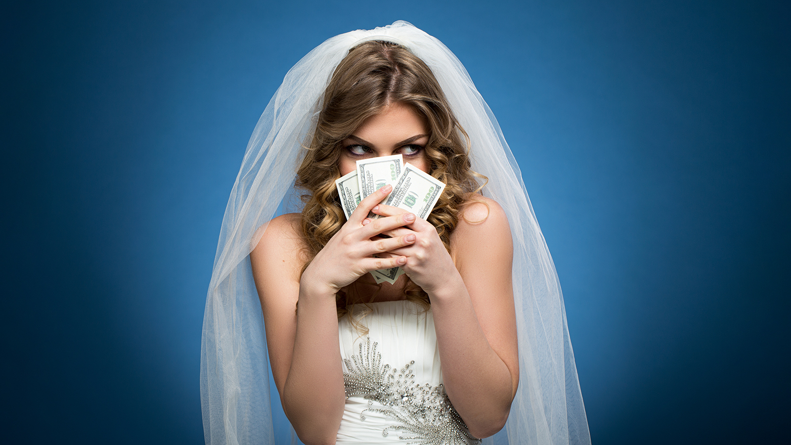 young beautiful girl in wedding dress veil with dollars in hands on blue background