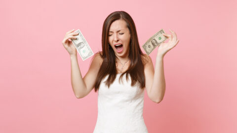 Portrait of dissatisfied bride woman in white wedding dress crying holding one dollar bills isolated on pastel pink background. Lack of money. Organization of wedding celebration concept. Copy space