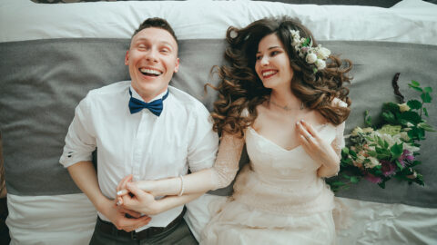 Stylish bride and groom are lying on the bed. Laughter and fun