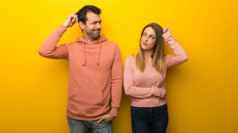 Group of two people on yellow background having doubts while scratching head