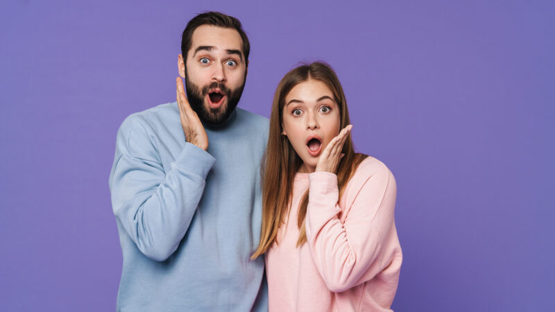 Photo of a shocked young loving couple isolated over purple background.