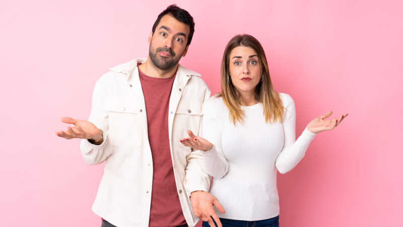 Couple in Valentine Day over isolated pink background having doubts while raising hands and shoulders