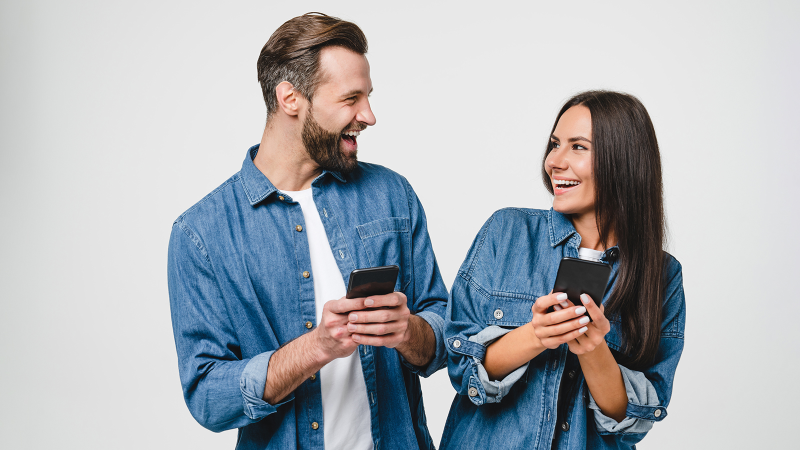 Young mobile users, loving couple spouses girlfriend and boyfriend using smart phones together looking at each other, surfing on internet online, e-commerce, e-banking isolated in white background