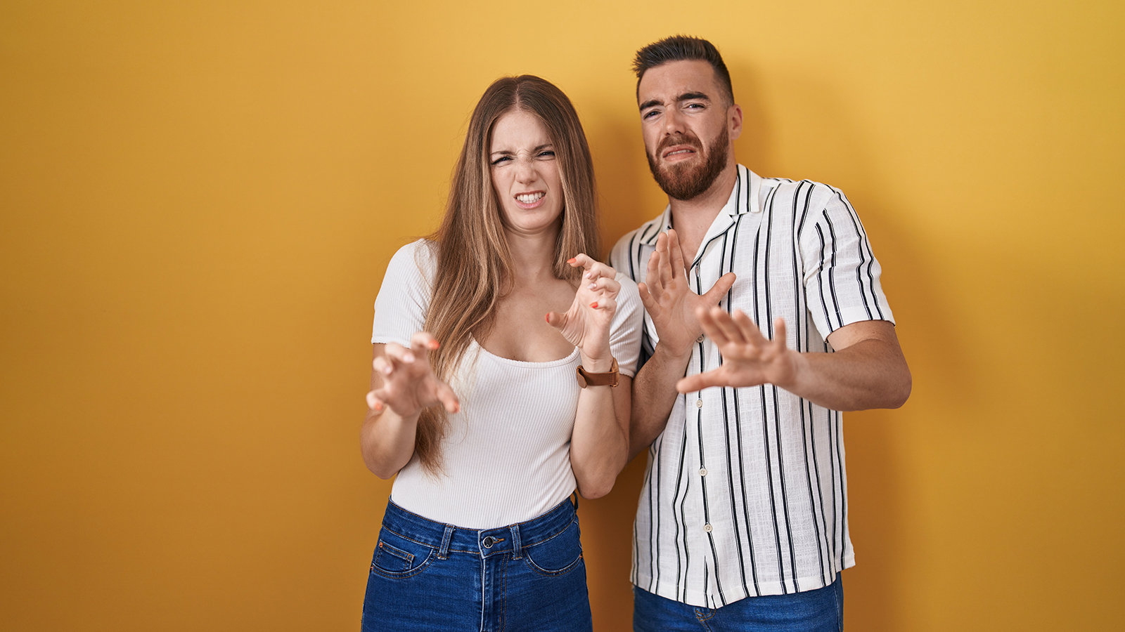 Young couple standing over yellow background disgusted expression, displeased and fearful doing disgust face because aversion reaction.