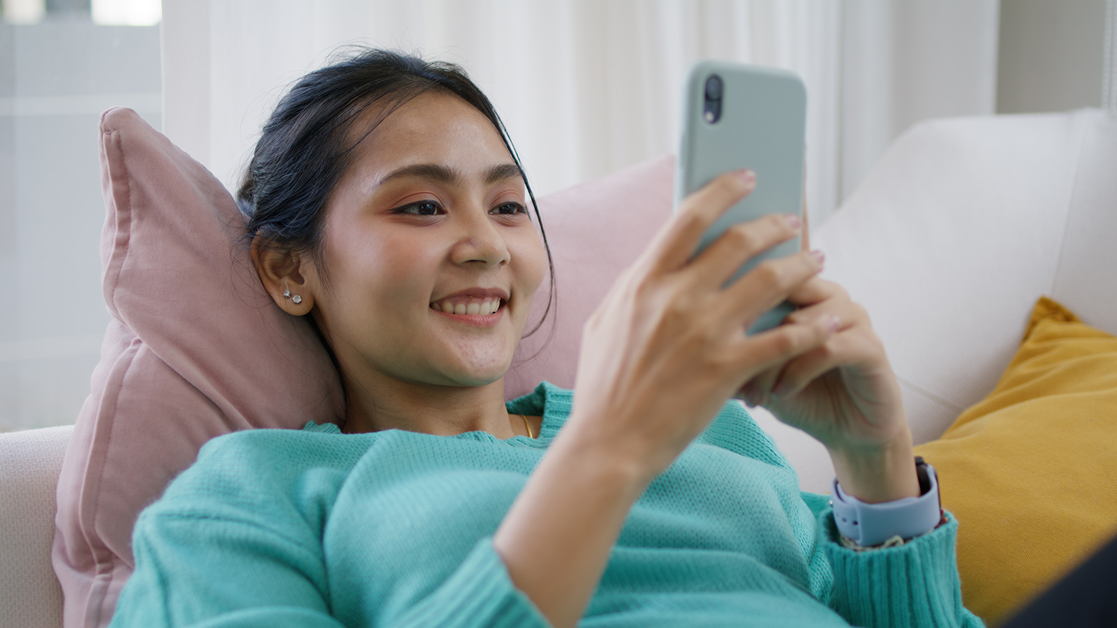 Young attractive beautiful casual asia female lady or student look at cellphone play social media IG reel tiktok app lying down at sofa couch living room feel relax comfort carefree at home apartment.
