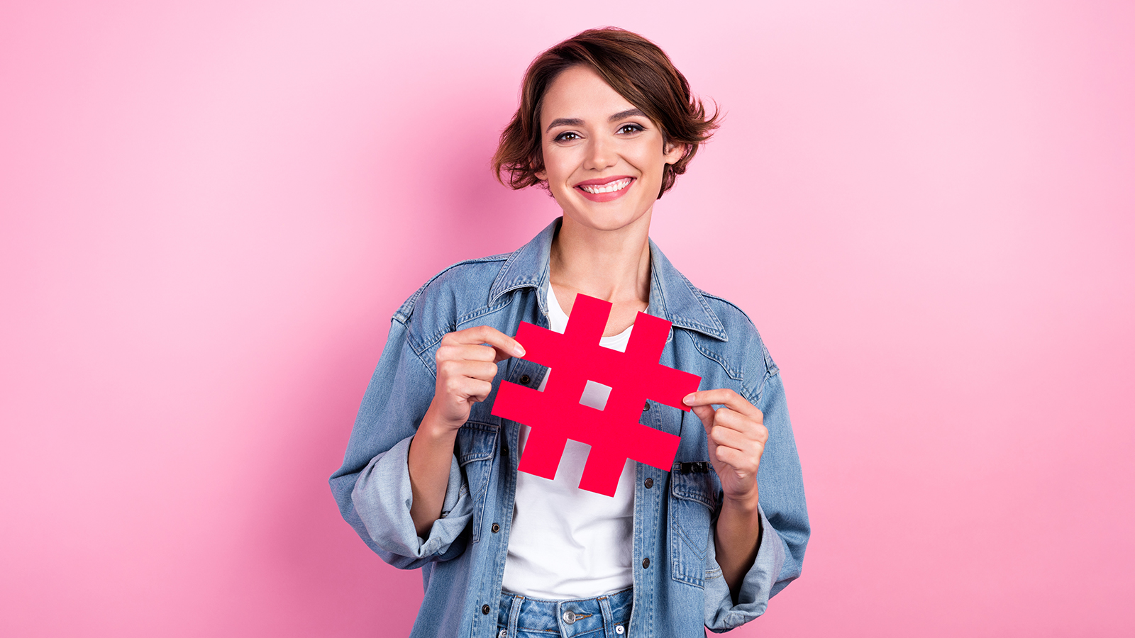 Portrait of cheerful lovely lady beaming smile hands hold show paper hashtag symbol card isolated on pink color background
