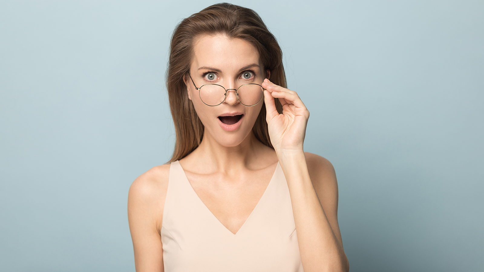 Surprised woman with open mouth in disbelief taking off glasses, hearing unexpected good news, astonished amazed female with wide open eyes looking at camera, isolated on studio background