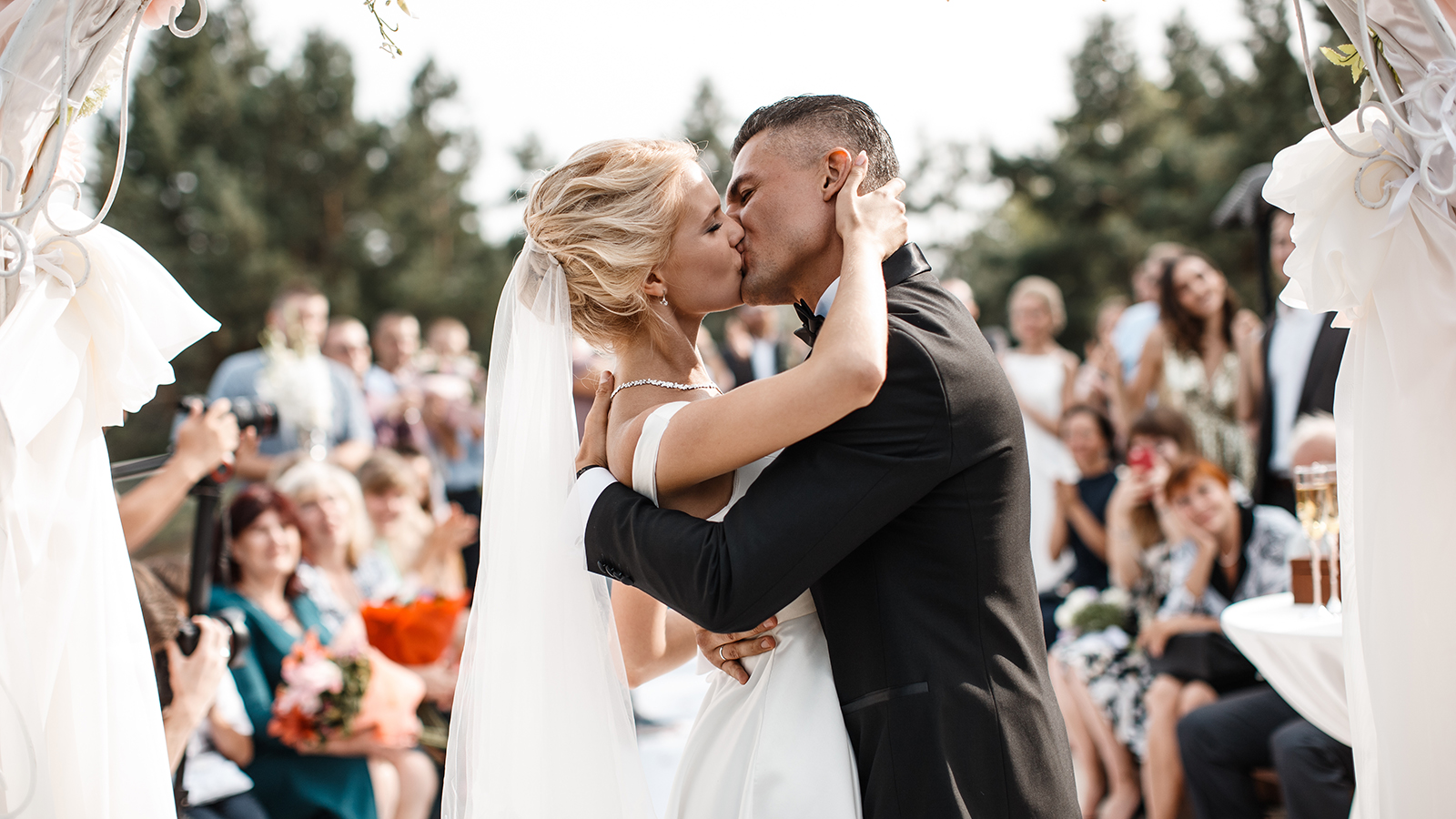 A bride and a groom are kissing in front of the guests.