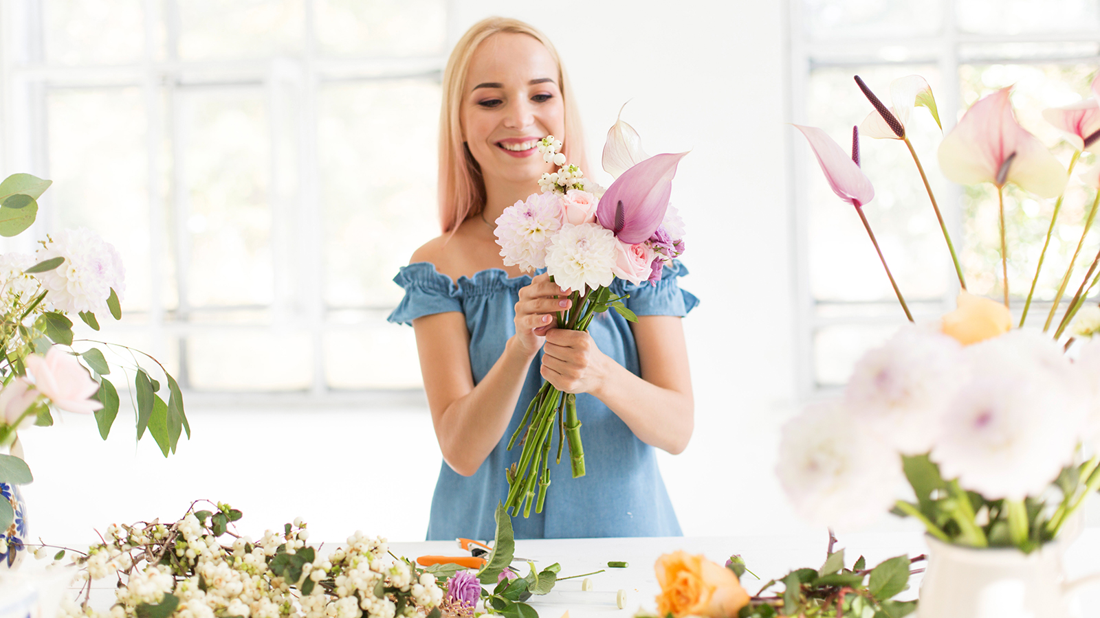 Girl florist at work. A beautiful girl creates a flower bouquet. Florist working table. A girl florist works in a white studio.