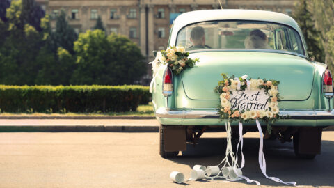 Wedding couple in car decorated with plate JUST MARRIED and cans outdoors