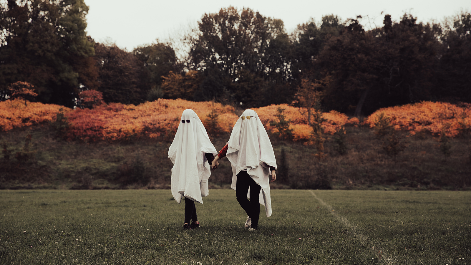 two friends dressed as ghosts are walking around the football stadium in the park