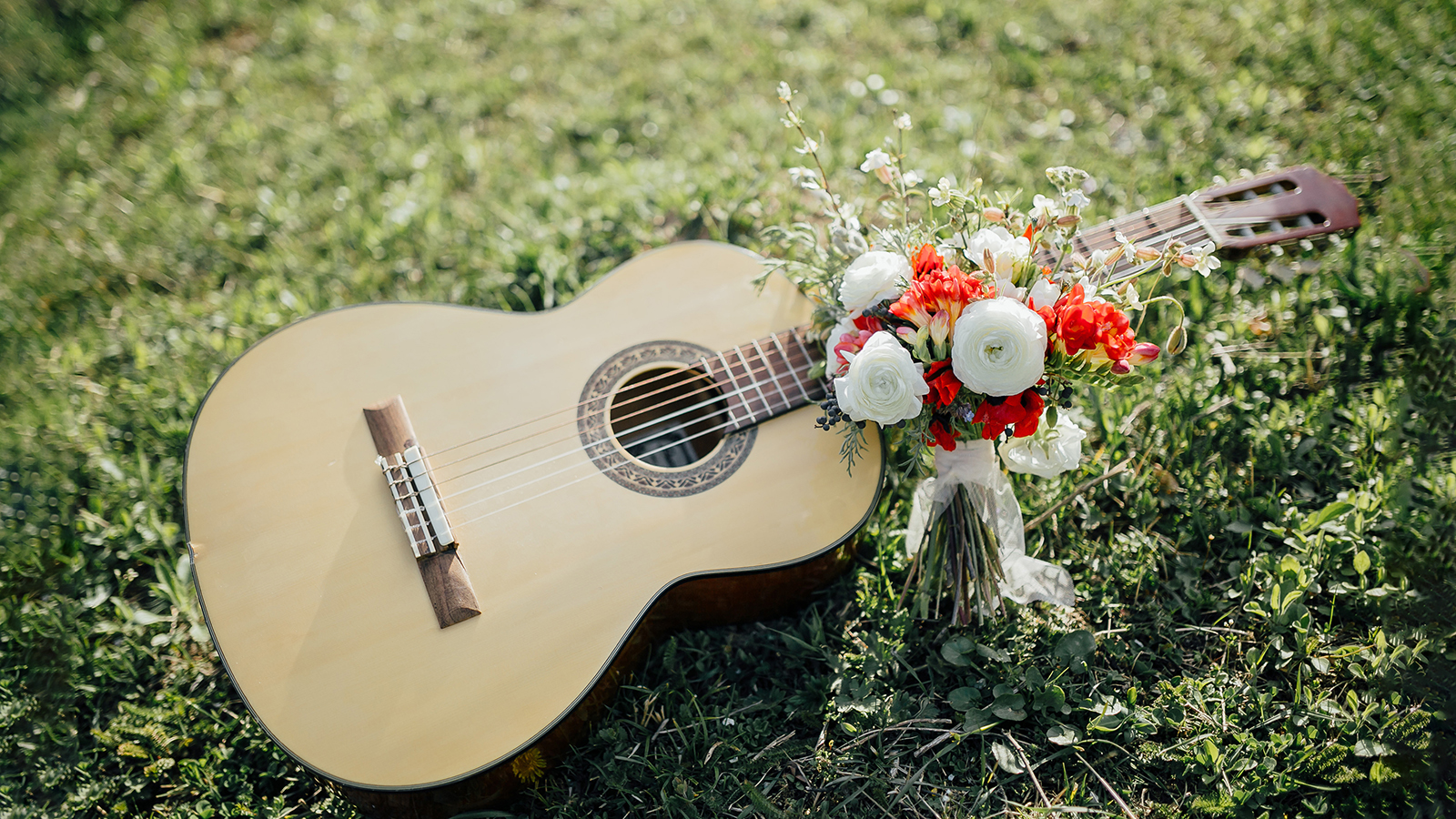 wedding bouquet of red and white flowers and greenery near a guitar on the green grass